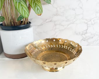May include: A gold-toned metal bowl with an intricate design and a scalloped edge. The bowl has a raised base and is perfect for serving snacks or fruit.
