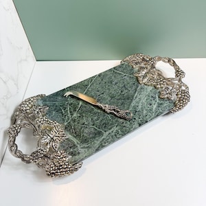 May include: A rectangular green marble serving tray featuring ornate silver-toned metal handles shaped like grape clusters and vine leaves, accompanied by a matching silver-toned cheese knife with a grape-themed handle design.