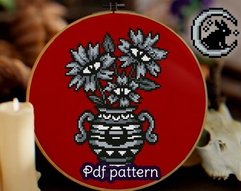 May include: A cross stitch pattern featuring a black and white vase with three stylized flowers with eyes. The vase and flowers are on a red background. The text "Pdf pattern" is at the bottom of the image.