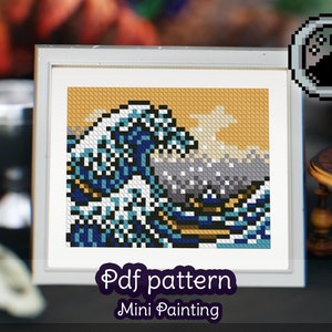 May include: A framed pixel art painting of the Great Wave off Kanagawa by Hokusai. The painting is in a white frame with a light yellow background. The text "Pdf pattern Mini Painting" is below the frame.