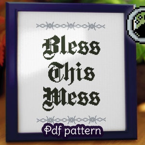 May include: A framed cross-stitch pattern with the text "Bless This Mess" in a gothic font. The frame is dark blue with a silver border. The pattern is on white fabric with black thread. The text "Pdf pattern" is printed below the cross-stitch.