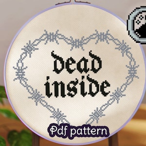 May include: Cross stitch pattern featuring the phrase "dead inside" in a gothic font, surrounded by a barbed wire heart. The pattern is displayed in a white embroidery hoop with a purple rim.