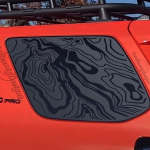 May include: A red Toyota 4Runner with a black "TRD PRO" emblem on the side. The rear window has a black topographic map decal applied to it. The decal is a popular design for off-road vehicles.