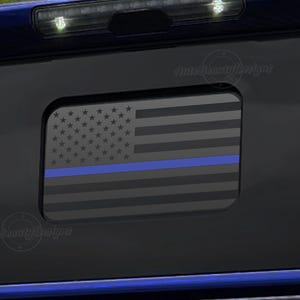 May include: A black and blue American flag with a thin blue line across the middle. The flag is on a black background.