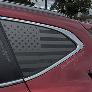 May include: A red car with a black and white American flag decal on the rear window. The decal is on the passenger side window and is visible from the outside of the car. The decal is a popular way to show patriotism and support for the United States.