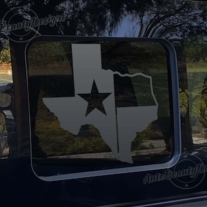 May include: A gray vinyl decal of the state of Texas with a white star and a white stripe across the middle. The decal is on a black car window.