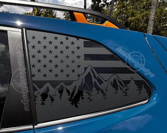 May include: A blue car with a black and white American flag and mountain scene decal on the back window. The decal features a silhouette of mountains, trees, and the American flag.