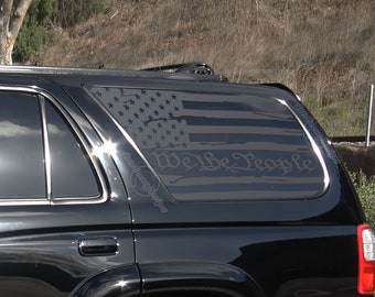 May include: A black SUV with a rear window decal of a distressed American flag with the words "We the People" in a script font.