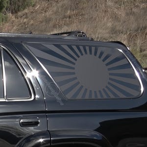 May include: Black SUV with a rear window decal of a rising sun graphic. The decal is in shades of gray and black.