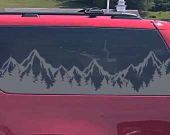 May include: A red SUV with a mountain range and pine trees silhouette decal on the rear window. The decal is in grey and is centred on the window. The decal says "Auto Beauty Designs" on the right side.