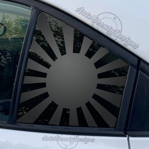 May include: A black and white rising sun graphic decal for a car window. The decal is applied to the rear passenger side window of a car. The decal is a popular design for car enthusiasts.