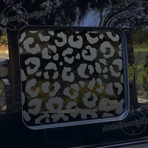 May include: A black car window with a gray and white leopard print decal. The decal is in the shape of a square and is centered on the window. The decal is a popular design for car windows and is a great way to add a touch of personality to your vehicle.