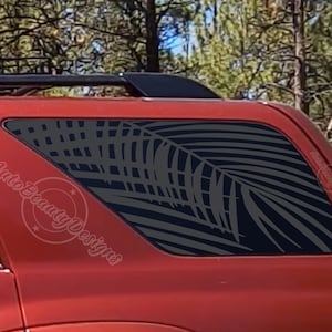 May include: A red SUV with a palm tree design on the rear window. The design is in a dark gray color and is visible through the tinted window. The text "Auto Beauty Designs" is visible on the side of the vehicle.