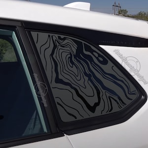 May include: A white car with a black window tint. The window tint has a black and gray abstract design.