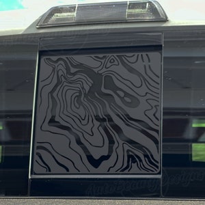 May include: A black and gray abstract pattern decal for a car window. The pattern resembles a topographic map.