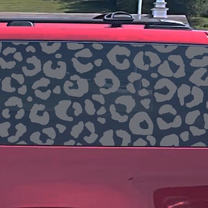May include: A red SUV with a leopard print window decal. The decal is gray and black and covers the entire back window. The decal says "Auto Beauty Designs" on the side.