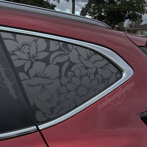 K&ouml;nnte beinhalten: Ein rotes Auto mit einer Fensterschutzfolie mit Blumenmuster. Die Folie ist dunkelgrau und zeigt ein gro&szlig;es Blumenmuster. Das Auto steht auf einer Auffahrt mit einem Haus im Hintergrund. Der Text "Auto Beauty Designs" ist auf der Autoscheibe sichtbar.