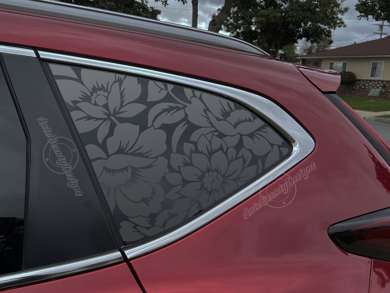 K&ouml;nnte beinhalten: Ein rotes Auto mit einer Fensterschutzfolie mit Blumenmuster. Die Folie ist dunkelgrau und zeigt ein gro&szlig;es Blumenmuster. Das Auto steht auf einer Auffahrt mit einem Haus im Hintergrund. Der Text "Auto Beauty Designs" ist auf der Autoscheibe sichtbar.
