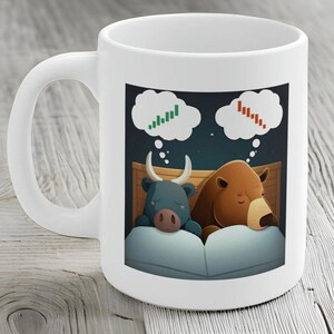 May include: White ceramic coffee mug with a cartoon illustration of a bull and a bear sleeping in a bed. The bull is dreaming of a green upward stock chart and the bear is dreaming of a red downward stock chart.