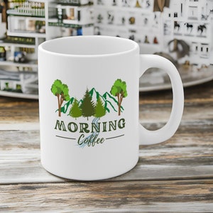 May include: White ceramic coffee mug with a green mountain scene and the text "MORNING Coffee" printed on it.