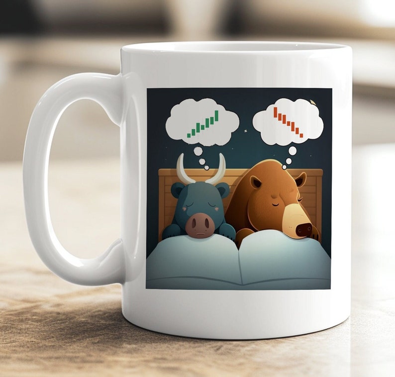 May include: White ceramic coffee mug with a cartoon illustration of a bull and a bear sleeping in a bed. The bull is dreaming of a green upward stock chart and the bear is dreaming of a red downward stock chart.