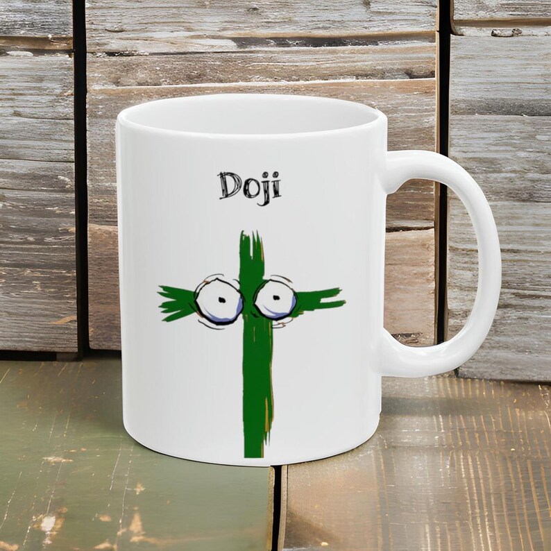 May include: White ceramic mug with a whimsical green cross design featuring cartoon eyes and the word "Doji" in black. The mug has a curved handle and is set against a wooden background.