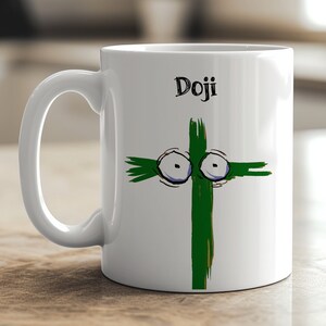May include: White ceramic mug with a whimsical green cross design featuring cartoon eyes and the word "Doji" in black script. The mug has a curved handle and is suitable for hot or cold beverages.
