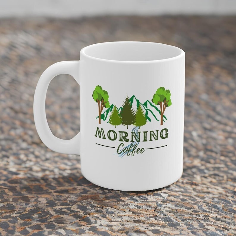 May include: White ceramic mug with a green mountain scene and trees. The text "Morning Coffee" is printed on the mug.