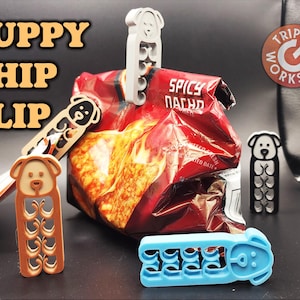 May include: Three different chip clips shaped like puppies. The clips are made of plastic and are in brown, blue, and gray. The text "PUPPY CHIP CLIP" is in the top left corner of the image. The text "TRIPLE G WORKSHOP" is in the top right corner of the image.