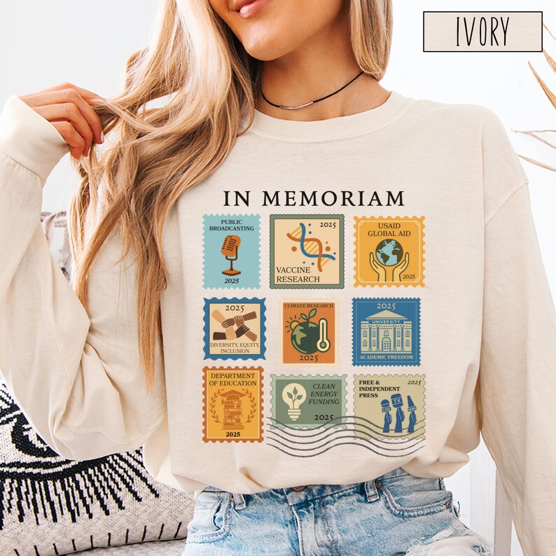 Pode incluir: Camiseta de manga comprida cor marfim com um gr&aacute;fico semelhante a um selo. O gr&aacute;fico inclui o texto "IN MEMORIAM" e v&aacute;rios selos com o ano "2025" e frases como "Public Broadcasting", "Vaccine Research" e "USAID Global Aid".