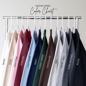 Puede incluir: Una carta de colores de sudaderas Gildan 18000 en varios colores, incluyendo blanco, arena, rosa claro, granate, azul claro, marino, verde bosque, chocolate, ceniza, gris deportivo, gris oscuro jaspeado y negro. Se muestra el texto "Color Chart".