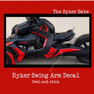 May include: Black and red Ryker three-wheeled motorcycle with a black seat. The motorcycle has red accents and the text "Ryker" on the side. The image also includes the text "The Byker Babe" and "Ryker Swing Arm Decal - Peel and stick."