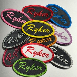 May include: A collection of oval-shaped embroidered patches with the word "Ryker" written in different colors and styles. The patches are made of black fabric with colorful embroidery.