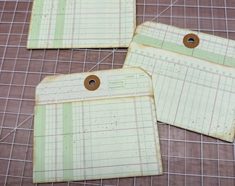 May include: Three rectangular paper tags with a vintage ledger design in pale green and cream. Each tag features a brown reinforced hole at the top, grid lines, and printed text including "Prepared By" and "Approved By" with ink-like speckles.