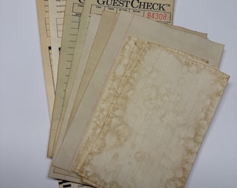 May include: A collection of vintage-style paper guest checks and lined stationery sheets. The papers have a tan, tea-stained appearance with visible brown blotches and aged textures. Some sheets display printed headers like GUEST CHECK and numbers.
