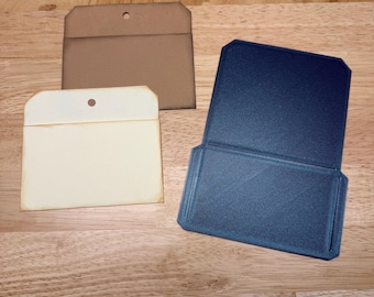 May include: Three rectangular card holders with clipped top corners. One holder is dark blue with a textured surface, one is light beige with a smooth finish, and one is brown with a smooth finish. Each holder features a small circular hole.