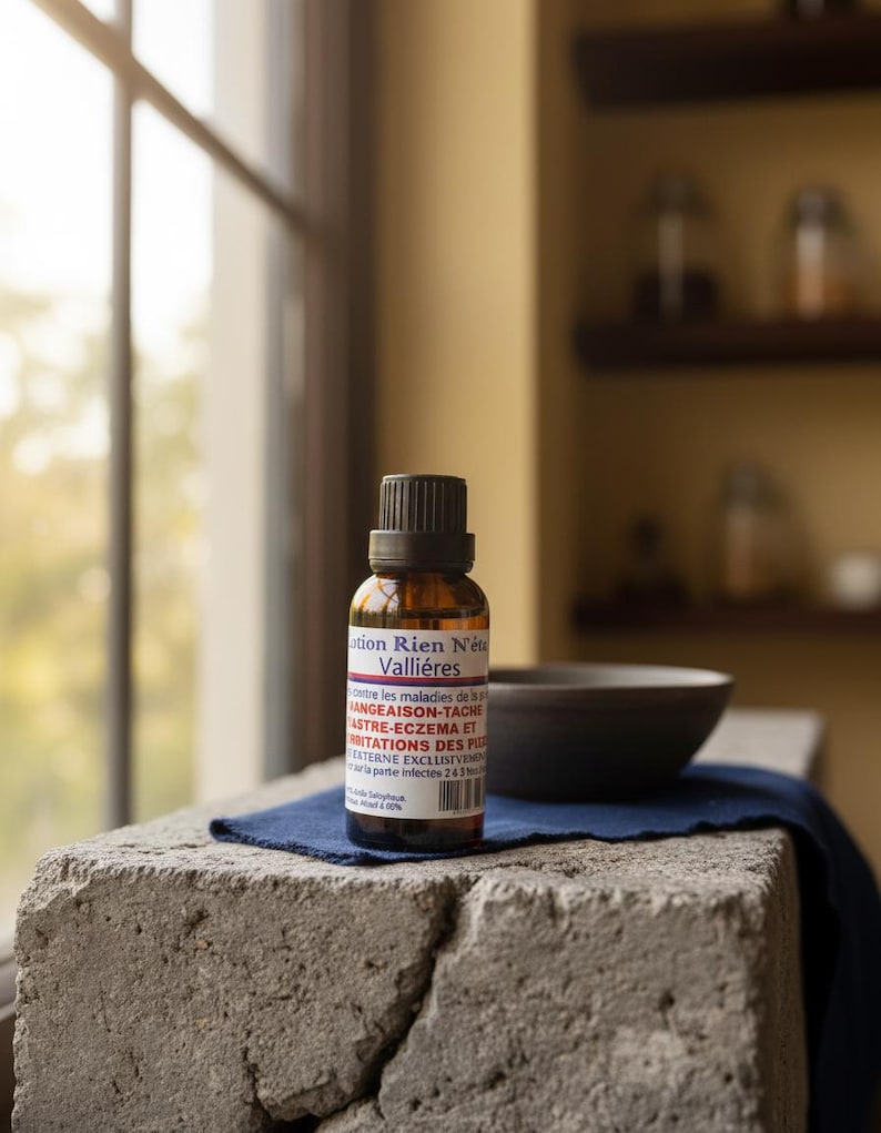 May include: A brown glass bottle with a black cap and a white and red label, next to a dark gray bowl. The bottle sits on a blue cloth atop a rough, gray stone surface, near a window.