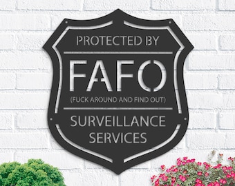 Può includere: Segno in metallo nero a forma di scudo con il testo "Protetto da FAFO (F**k Around and Find Out) Servizi di sorveglianza".