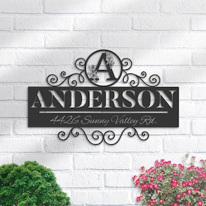 May include: Black metal house sign with a decorative scroll design. The sign features the name "ANDERSON" and the address "4426 Sunny Valley Rd.". The letter "A" is in a circle with floral accents.