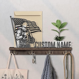 May include: A wooden shelf with hooks, holding a tote bag, keys, and a scarf. Above, a metal cutout depicts a basketball player with an American flag. The words "CUSTOM NAME" are displayed on the shelf.