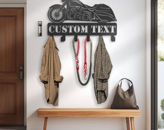 Könnte beinhalten: Schwarzer Motorrad-Wandhaken aus Metall mit vier Haken und dem Text "CUSTOM TEXT". Der Haken ist an einer weißen Wand über einer Holzbank montiert. An den Haken hängen zwei Mäntel und eine Tasche.