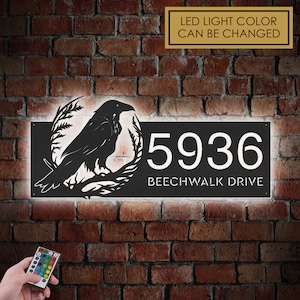 Può includere: Cartello per numeri civici in metallo nero con una silhouette di corvo e le parole "Beechwalk Drive" e il numero "5936". Il cartello è illuminato da luci LED bianche che possono essere cambiate con un telecomando.