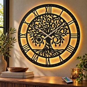 Könnte beinhalten: Eine große, runde, schwarze Wanduhr mit einem lasergeschnittenen Lebensbaum-Motiv in der Mitte, ergänzt durch Sonnen- und Mondsymbole. Das Zifferblatt zeigt römische Ziffern und wird von einem warmen LED-Lichtring von hinten beleuchtet.