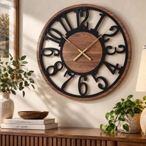 May include: A round wall clock featuring a dark wood grain centre and a black metal outer ring with large, stylised black numerals. The clock has two thin, gold-coloured metal hands positioned against the wood background, creating a contrast.