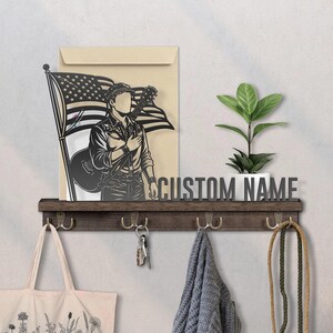 May include: A dark wooden shelf with hooks, displaying a decorative piece with a guitar player and an American flag. A plant in a white pot and the text "CUSTOM NAME" are also on the shelf. A tote bag, keys, and a scarf hang below.