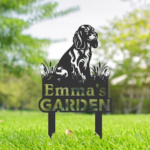May include: Black metal garden stake with a silhouette of a dog sitting in tall grass. The stake has the text "Emma's Garden" on it.