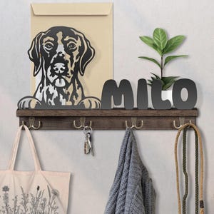May include: A wooden wall shelf with a metal dog silhouette, the name "MILO", and hooks. A plant in a white pot sits on the shelf. A tote bag, keys, a scarf, and a leash hang below.