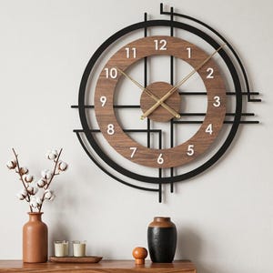 May include: A round wall clock featuring a dark brown wood-grain circular face with white numerals from 1 to 12. The clock is framed by a black metal geometric structure with intersecting lines and circles, complemented by thin gold-colored hands.