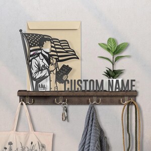 May include: A wooden wall shelf with hooks, a plant, and a decorative cutout of a doctor holding an American flag. The shelf has the text "CUSTOM NAME" and is adorned with a tote bag, keys, and a scarf.