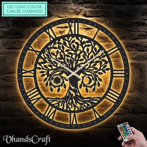 May include: Black metal wall clock with a tree of life design and Roman numeral markings. The clock has a built-in LED light that can be changed to different colors using a remote control. The text "LED light color can be changed" is visible in the image.